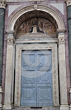 Wooden door, light colored colored surrounded by an important white marble frame in the church of Santa Maria in Florence.