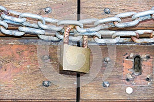 A wooden door locked with a chain and a rusty padlock