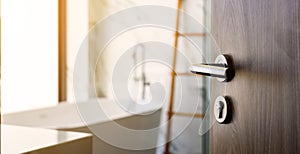 Wooden door open to nice modern bathroom, marble walls. selective focus to door handle, bathroom and bathtub blurred on background