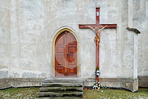 Wooden door to the church and a big cross on the wall. Lighted candles. Christian tradition.