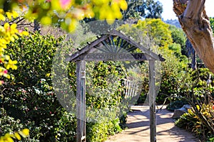 A wooden doorway with a dirt path to the discovery garden surrounded by lush green plants and trees