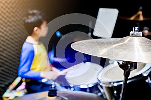 Wooden drumsticks in hands of Asian kid wearing blue and yellow t-shirts to learning and play drum set in music room