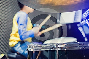 Wooden drumsticks in hands of Asian kid wearing blue and yellow t-shirts to learning and play drum set in music room