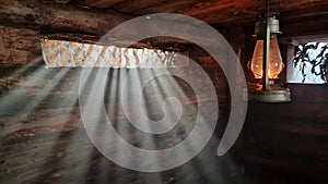 A wooden dugout in which a kerosene lamp burns. Light from the window penetrates into the room.