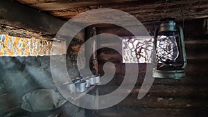 A wooden dugout in which a kerosene lamp burns. Light from the window penetrates into the room.