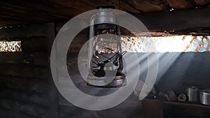 A wooden dugout in which a kerosene lamp burns. Light from the window penetrates into the room.