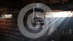 A wooden dugout in which a kerosene lamp burns. Light from the window penetrates into the room.