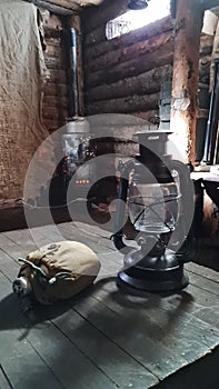 A wooden dugout in which a kerosene lamp burns. Light from the window penetrates into the room.