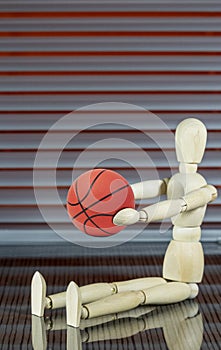 Wooden dummy with basketball in front of a jalousie plays with the ball