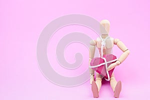 Wooden dummy chaining themselves to the paper box red heart shape on pink background with copy space for your