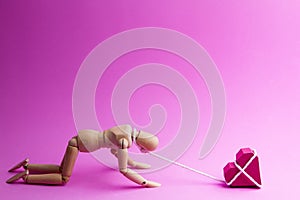 Wooden dummy chaining themselves to the paper box red heart shape on pink background with copy space for your