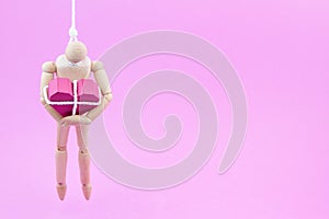 Wooden dummy chaining themselves to the paper box red heart shape on pink background with copy space for your
