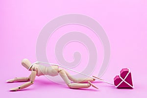 Wooden dummy chaining themselves to the paper box red heart shape on pink background with copy space for your