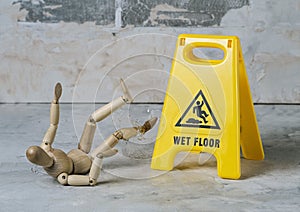 wooden dummy slipped and fell in a puddle with splashing water near a warning sign wet floor