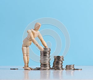 Wooden dummy and stacks of white coins, the concept of accumulation of cash, donation, subsidy