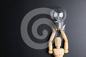 Wooden dummy toy and light bulb on black background with copy sp