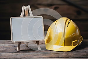 Wooden easel displays safety messages near yellow hard hat for workplace awareness