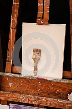 Wooden easel with one white canvas one used paintbrush