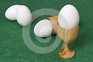 Wooden egg cup holder with white egg on green table