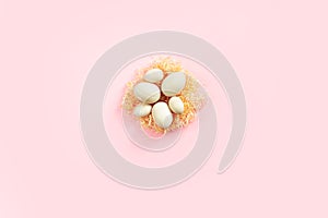 Wooden eggs lying on artificial nest in the center on pink background. Easter eco-friendly concept