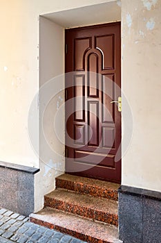 Wooden elegant entrance door with stone red granite threshold and steps at the facade of the building with peeling plaster