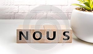 Wooden elements cubes with letters and the word NOUS on a light table against a brick wall, business concept and WAY OF