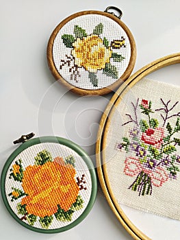Wooden embroidery hoops, scissors, needle, thread and fabric with floral cross-stitch embroidery on white