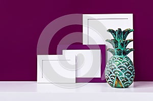 Wooden empty frames for a photo and a wooden emerald pineapple on a white shelf on a background of a bright purple red