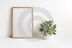 Wooden empty picture frame leaning on white wall next to small succulent houseplant. Poster mockup