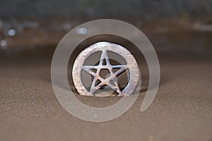 Wooden encircled Pentagram symbol on the beach at sunrise in front of the lake. Concept of Five elements: