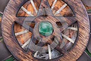 Wooden encircled Pentagram symbol with Green Aventurine in the middle of a circle made of colorful parrot feathers. Five elements