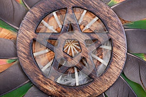 Wooden encircled Pentagram symbol in the middle of a circle made of colorful parrot feathers. Five elements