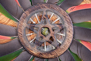 Wooden encircled Pentagram symbol with Unakite stone in the middle of a circle made of colorful parrot feathers. Five elements