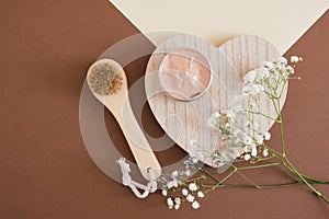 wooden face massage brush, blank mock up aluminum open cosmetic cream jar with pink clay mask and lily flowers
