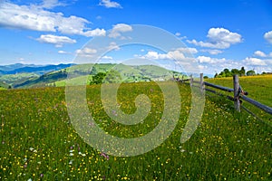 Wooden fence across mountain pasture, blue sky with clouds. Ukraine, carpathians.