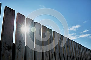 Wooden fence on a background of blue sky with clouds on a sunny day. Rustic wooden plank background