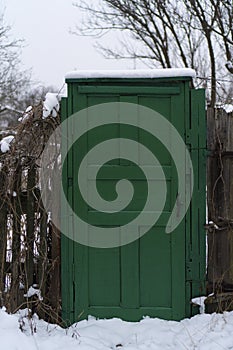 Wooden fence with beautiful classic green wooden entrance door with handle. The door covered with snow on the park. The old vintag