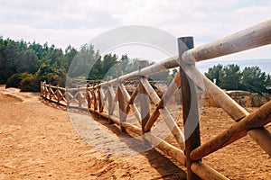 Wooden fence on the coast of Benagil beach in Portugal. View of the coniferous forest on a clear day