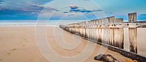 Wooden fence on empty beach at sunset