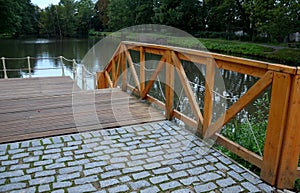 Wooden fence made of beams painted brown and screwed into the shape of an x cross at the shore of a pond with a floating plank p