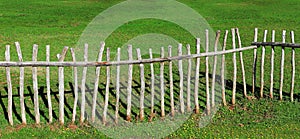 Wooden fence made of logs, against green grass