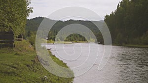 Wooden fence is on one side of large river, trees and mountain on other.