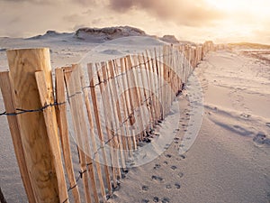 Wooden fence on a sand dune and animal footprints. Sunset sky in the background. Stunning nature scene. Dog`s bay, county Galway,