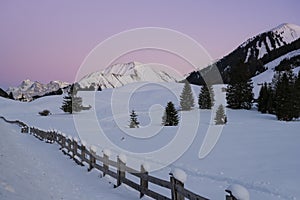 Wooden fence with snow hoods on pillars and a beautiful snow landscape in the mountains