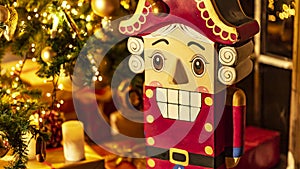 Wooden festive toy nutcracker on the background of a Christmas tree, gifts, lights, candles. Christmas and New Year interior