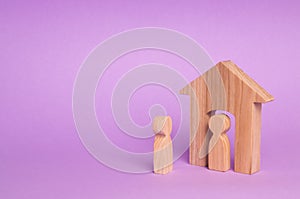 A wooden figure of a man meets a guest on a purple background. Wooden house. The concept of an apartment house, real estate.