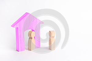 A wooden figure of a man meets a guest on a white background. Pink house. The concept of an apartment house, real estate.