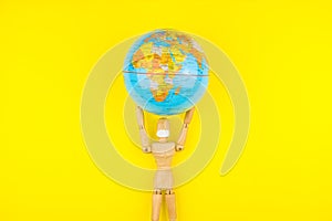 Wooden figure mannequin carrying planet earth globe over head on a yellow background