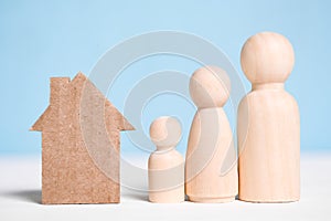 Wooden figures family with cardboard house on blue background