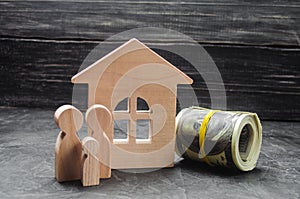 Wooden figures of the family stand near a wooden house and collapsed money. Buying and selling a house. Good life, moving